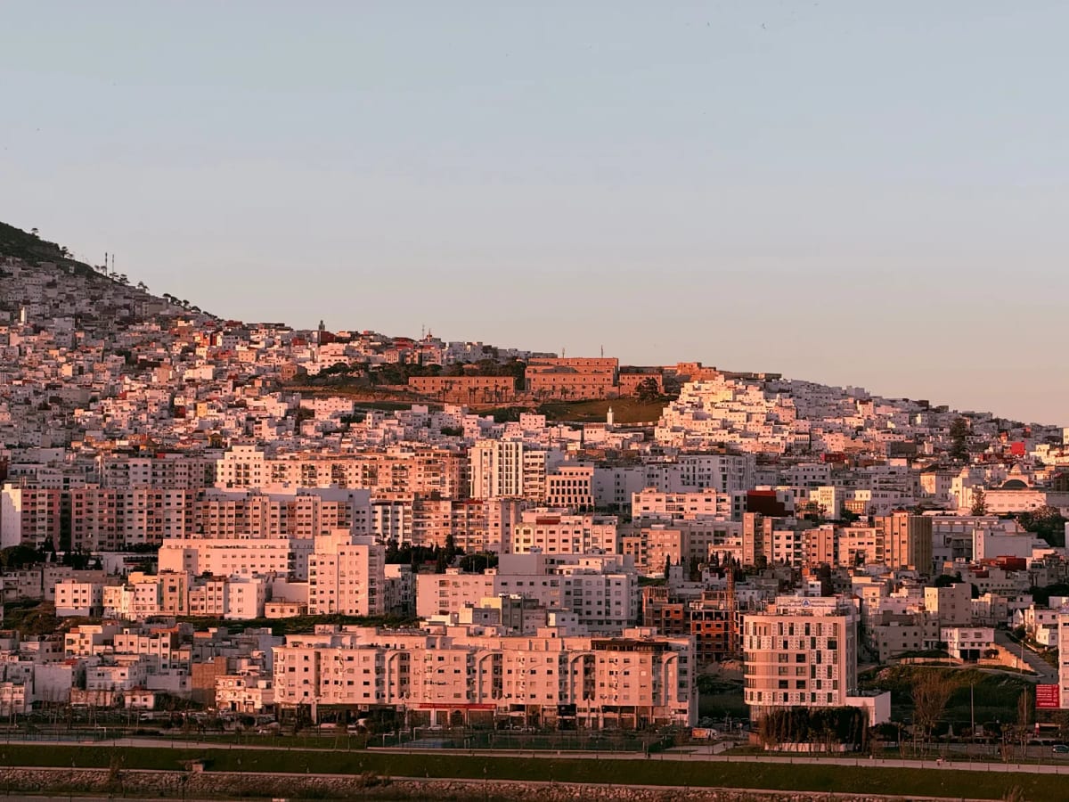 Immeubles résidentiels couvrant une colline de Tanger, éclairés en rose par le soleil couchant