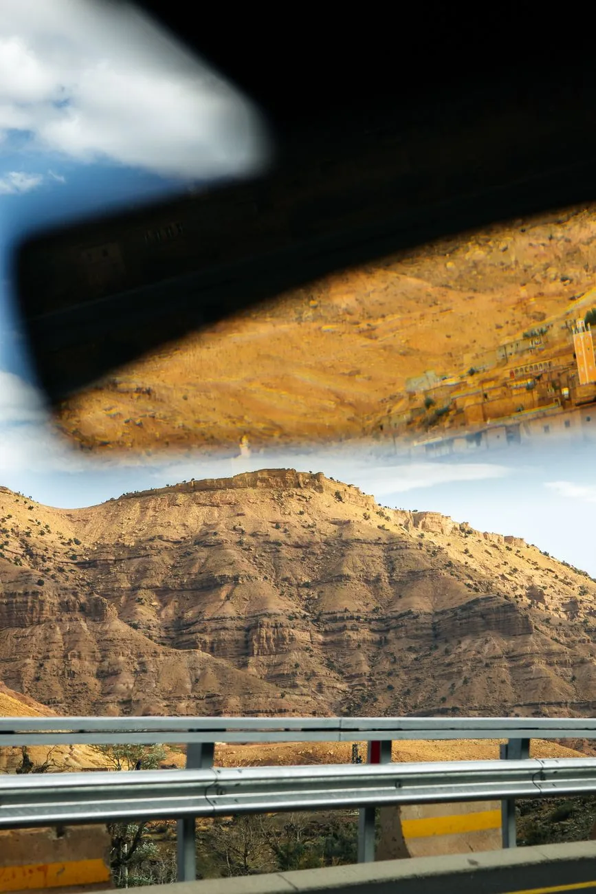 Rétroviseur d’une voiture reflétant une route de montagne et un paysage ocre au Maroc