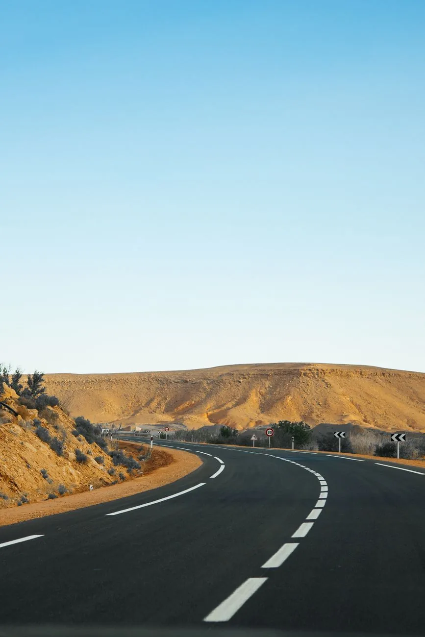Route asphaltée filant droit vers des collines ocres sous un ciel dégagé, au Maroc