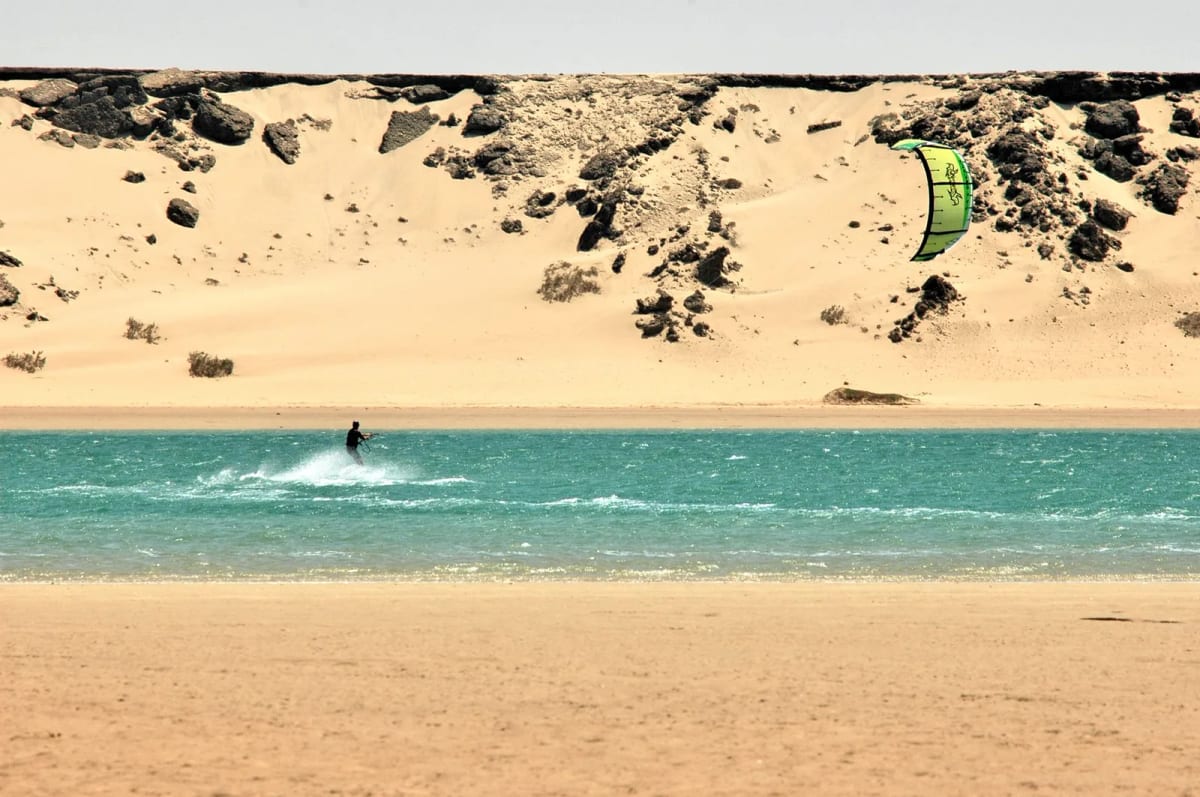 Kitesurfeur sur l’eau turquoise de la lagune de Dakhla, devant les dunes du Sahara atlantique