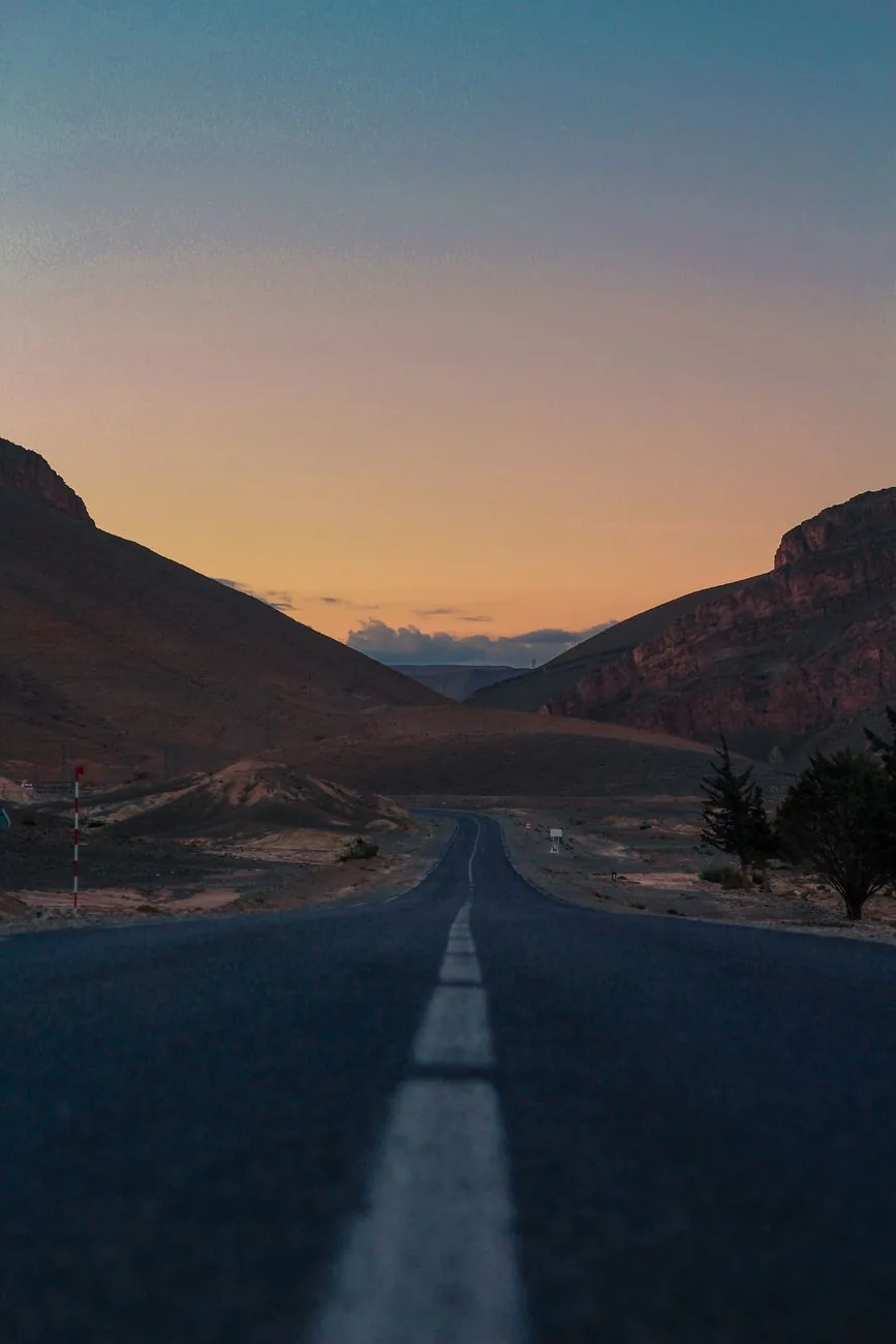 Route asphaltée filant entre des montagnes au crépuscule, au Maroc