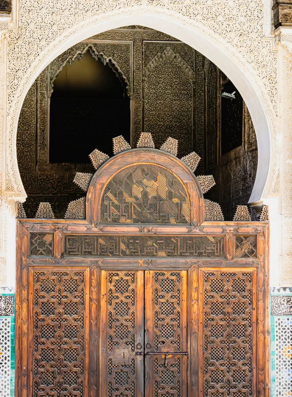 Porte de cèdre sculpté sous un arc en fer à cheval dans une médersa de Marrakech