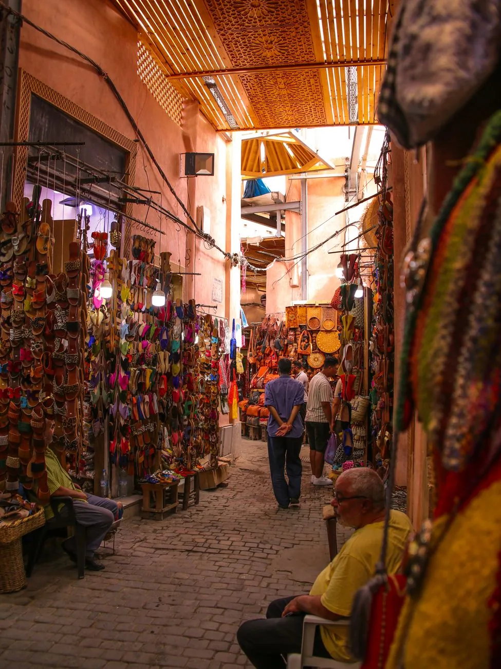 Ruelle de souk à Marrakech, échoppes d’artisanat et passants sous les claustras