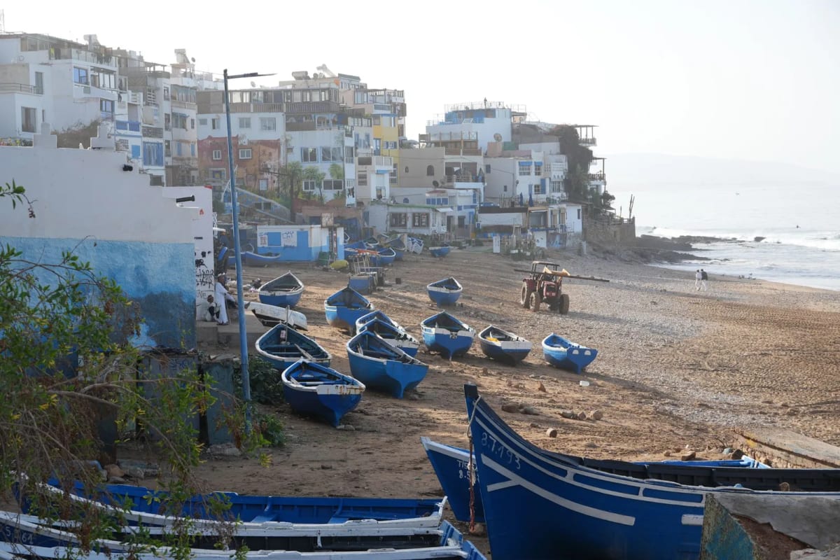 Plage du village de Taghazout avec barques de pêche bleues échouées sur le sable et maisons blanches