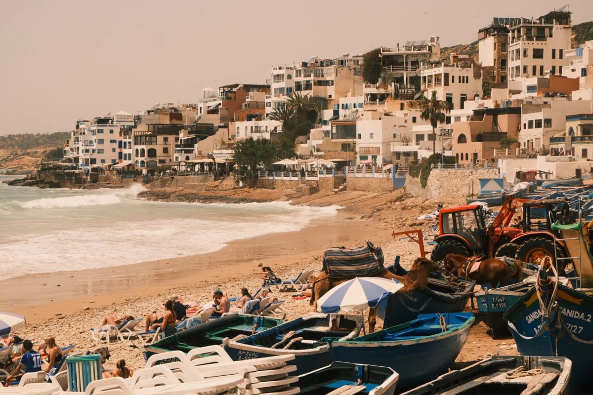Village de Taghazout, maisons blanches étagées sur la colline au-dessus de la plage et des barques de pêche bleues